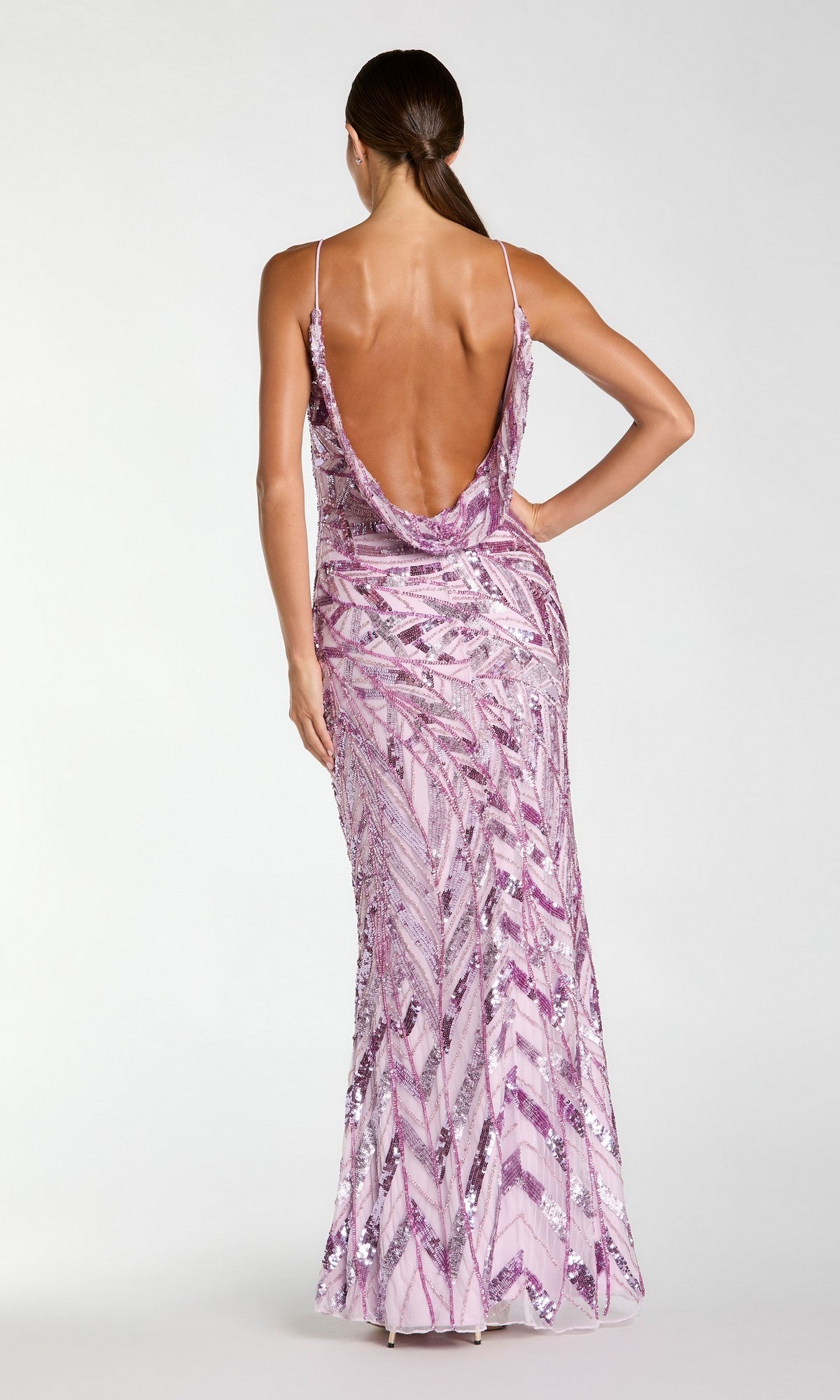 A woman stands with her back to the camera, showcasing the Long Formal Dress: Mac Duggal 6214—a floor-length, backless gown adorned with pink sequins, featuring thin straps and a striking geometric pattern. This glamorous dress effortlessly combines sparkling embellishments with refined elegance for an unforgettable look.